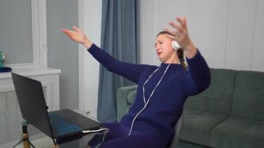 Çevrimiçi oyun oynayan, kulaklık takan, sanal dünyada gezinen, dağınık yatak odası ortamında laptop ve fare kullanan genç bir kadın.