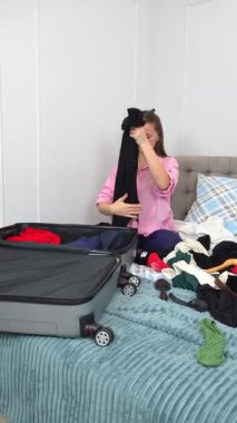 Dişi gezgin giysileri düzenler ve yatakta otururken düzgünce katlar, yaklaşan gezi için bavulu dikkatlice hazırlar, dikkatlice kıyafetleri seçer ve özenle hazırlar.