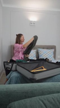 Dişi gezgin giysileri düzenler ve yatakta otururken düzgünce katlar, yaklaşan gezi için bavulu dikkatlice hazırlar, dikkatlice kıyafetleri seçer ve özenle hazırlar.