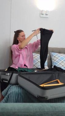 Dişi gezgin giysileri düzenler ve yatakta otururken düzgünce katlar, yaklaşan gezi için bavulu dikkatlice hazırlar, dikkatlice kıyafetleri seçer ve özenle hazırlar.