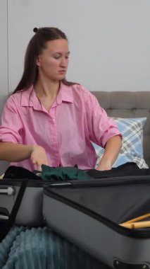 Dişi gezgin giysileri düzenler ve yatakta otururken düzgünce katlar, yaklaşan gezi için bavulu dikkatlice hazırlar, dikkatlice kıyafetleri seçer ve özenle hazırlar.