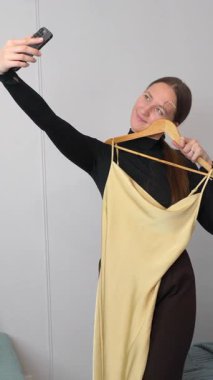 Çevrimiçi giyim perakendecisi, beyaz arkaplana karşı ahşap askıdaki sarı ipek elbiseyi fotoğraflayarak e-ticaret platformu dikey video için görsel içerik oluşturuyor