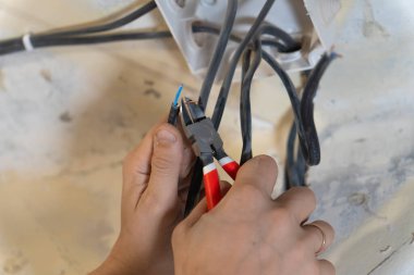 Elektrikçi, elektrik sistemindeki güvenli ve verimli bağlantıları sağlamak için penseyi ustalıkla keserek elektrik kablolarını soyuyor, hayati bakım ve montaj işlerini yapıyor.