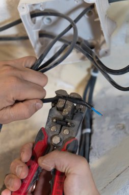 Elektrikçi, elektrik kablosundan yalıtım malzemelerini dikkatlice çıkarmak için kablo sökücüleri kullanıyor ve onu bir ev yenileme projesi sırasında bağlantı için hazırlıyor. Dikey fotoğraf