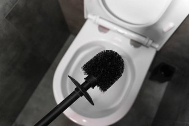 Modern siyah tuvalet fırçası açık beyaz bir klozetin üzerinde süzülüyor, modern bir banyoda temizliğe hazırlanıyor.
