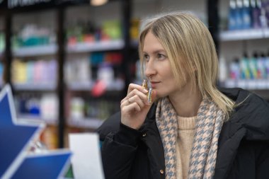 Sarışın kadın güzellik salonundaki parfüm testçisinin kokusundan zevk alıyor. Raflardaki çeşitli ürünlerden kendine özel bir koku seçiyor.