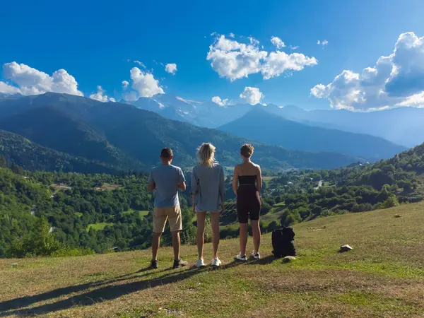 Üç turist, Gürcistan 'ın pitoresk manzaraları ve yürüyüş yolları ile tanınan ve güneşli bir günde doğanın güzelliğini alan Svaneti' de çarpıcı bir dağ manzarasının keyfini çıkarıyorlar.