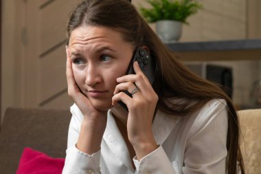Genç bir kadın telefon görüşmesi sırasında üzücü haberler alırken endişeli görünüyor, dikkatle dinlerken yüzü endişeli ve stresli görünüyor.