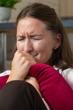 Üzgün kadın yüzünü yastığa saklarken ağlıyor, evdeki kahverengi bir kanepede oturuyor, depresyon ve yalnızlık hisleriyle boğuşuyor, derin duygusal acılar yaşıyor. Dikey fotoğraf