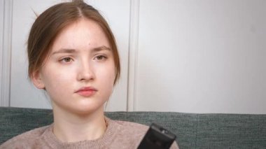 Rahat genç bir kız rahat bir koltukta oturuyor TV kanallarını değiştiriyor evinde kablosuz uzaktan kumandayla eğleniyor.