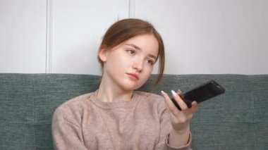 Rahat genç bir kız rahat bir koltukta oturuyor TV kanallarını değiştiriyor evinde kablosuz uzaktan kumandayla eğleniyor.