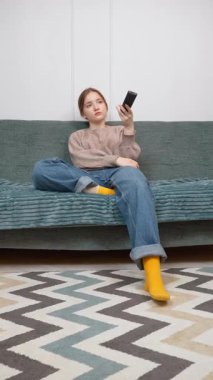 Rahat genç kız boş zamanlarını kanepede oturup televizyon izleyerek geçirmeyi seviyor. Uzaktan kumandayı kullanarak loş ışıklı oturma odasının dikey görüntülerini değiştiriyor.