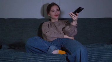 Rahat genç kız boş zamanlarını kanepede oturup televizyon izleyerek geçirmeyi ve loş ışıklı oturma odasındaki kanalı değiştirmek için uzaktan kumandayı kullanmayı seviyor.