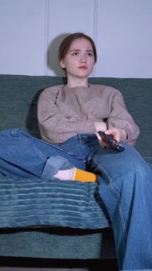 Rahat genç kız boş zamanlarını kanepede oturup televizyon izleyerek geçirmeyi seviyor. Uzaktan kumandayı kullanarak loş ışıklı oturma odasının dikey görüntülerini değiştiriyor.