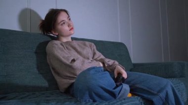 Sıkıntı ve ilgisizlik, genç bir kadını elinde uzaktan kumandayla koltuğunda otururken oturma odasının loş ışığında televizyona bağlanacak bir şey bulmak için çırpınırken tüketir.