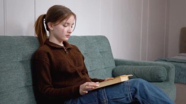 Genç kız öğrenci, rahat oturma odasında kanepede oturmuş edebiyattan gelen mutluluk ve hazzı gösterirken zevkle kitap okuyor. Gülümsüyor