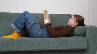 Kaygısız genç kız dairedeki kanepede kitap okuyor. Edebiyat ve okuma, bir öğrenci olarak sınavlara hazırlanıyor ya da okul müfredatını okuyor..