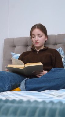 Rahat genç kız öğrenci rahat bir yatakta dinlenirken kitap okuyor, sessiz bir çalışma sırasında el yazısıyla notlar almak için ara sıra duruyor.