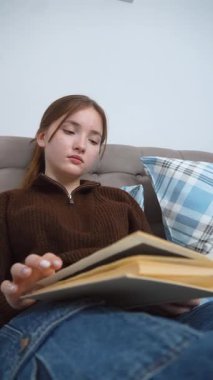 Rahat giysiler içinde genç bir kız öğrenci. Kareli yastıklarla uzanmış kitap okuyor, sayfaları değiştiriyor ve dinlenme ve ders çalışmanın tadını çıkarıyor.