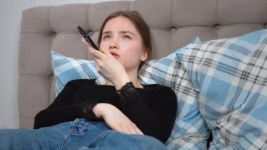 Rahat genç bir kadın, rahat bir şekilde yatakta uzanıyor, akıllı telefondan sesli mesaj kaydediyor, sakin bir dijital bağlantı ve rahatlama anının tadını çıkarıyor.