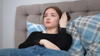 Rahat genç bir kadın, rahat bir şekilde yatakta uzanıyor, akıllı telefondan sesli mesaj kaydediyor, sakin bir dijital bağlantı ve rahatlama anının tadını çıkarıyor.