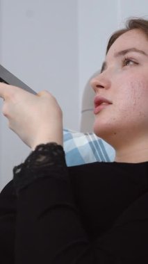 Genç bir kadın bir yastıkla yatakta uzanıyor, akıllı telefonunu kullanıyor, kulağına tutmakla, dinlemeyi önermek ve uzak tutmak arasında değişiyor, konuşmayı veya hoparlörü kullanmayı öneriyor.