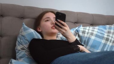 Yatakta rahat rahat uyuyan, sosyal medyada gezinen, mesajlaşan ve rahat ev ortamında dijital içerikle meşgul olan kadın.