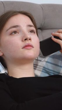 Rahat giyinen, yatakta dinlenen, sosyal medyada gezinirken akıllı telefon kullanan, mesajlaşan ve rahat ev ortamında dijital içerikle ilgilenen bir kadın.