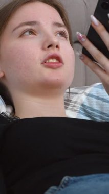 Rahat bir kanepede dinlenen genç bir kadın rahat bir evde rahat rahat el hareketleriyle sesli video kaydediyor.