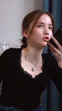 Genç kız akıllı telefonu yüze yakın tutuyor, sesli mesajlar kaydediyor ya da elleriyle konuşmuyor. Akıllı telefondaki sesli asistanı olan kadın rahat beyaz mutfak mobil iletişim uygulamasında