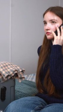 Heyecanlı genç kız bavulunun yanında oturuyor, telefon görüşmesi duygusal bir yolculuğa hazırlanıyor, yaklaşan yolculuk videosundan korkuyor.