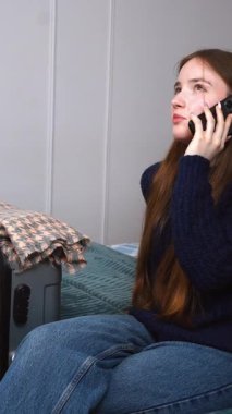 Heyecanlı genç kız bavulunun yanında oturuyor, telefon görüşmesi duygusal bir yolculuğa hazırlanıyor, yaklaşan yolculuk videosundan korkuyor.