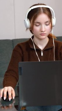 Oturma odasındaki cam masada kulaklık ve fare kullanarak uzaktan bilgisayarla çalışan odaklı serbest çalışan genç kız. Bilgisayar oyunu oynuyordum. dikey video