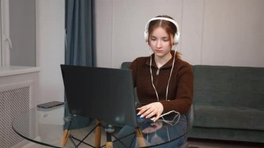 Oturma odasındaki cam masada kulaklık ve fare kullanarak uzaktan bilgisayarla çalışan odaklı serbest çalışan genç kız. Bir bilgisayar oyunu oynuyorum.