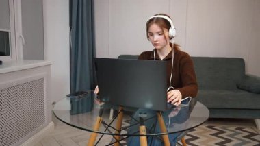 Oturma odasındaki cam masada kulaklık ve fare kullanarak uzaktan bilgisayarla çalışan odaklı serbest çalışan genç kız. Bir bilgisayar oyunu oynuyorum.