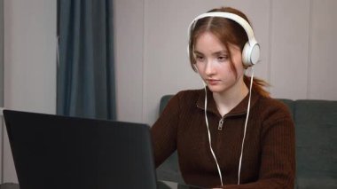 Oturma odasındaki cam masada kulaklık ve fare kullanarak uzaktan bilgisayarla çalışan odaklı serbest çalışan genç kız. Bir bilgisayar oyunu oynuyorum.