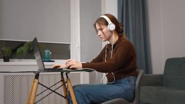 Hedef odaklı genç serbest yazar uzaktan bilgisayarda çalışıyor kulaklıkla müzik dinliyor oturma odasındaki küçük masada oturmuş bilgisayar oyunu oynuyor.