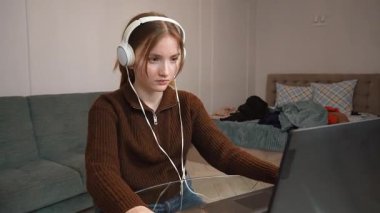 Hedef odaklı genç serbest yazar uzaktan bilgisayarda çalışıyor kulaklıkla müzik dinliyor oturma odasındaki küçük masada oturmuş bilgisayar oyunu oynuyor.