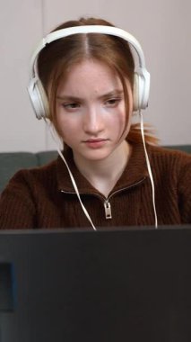 Hedef odaklı genç serbest yazar uzaktan bilgisayarda çalışıyor kulaklıkla müzik dinliyor bilgisayar oyunu oynuyor oturma odasındaki küçük masada dikey video odasında oturuyor.