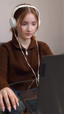 Hedef odaklı genç serbest yazar uzaktan bilgisayarda çalışıyor kulaklıkla müzik dinliyor bilgisayar oyunu oynuyor oturma odasındaki küçük masada dikey video odasında oturuyor.