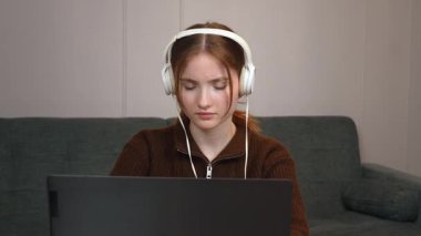 Hedef odaklı genç serbest yazar uzaktan bilgisayarda çalışıyor kulaklıkla müzik dinliyor oturma odasındaki küçük masada oturmuş bilgisayar oyunu oynuyor.