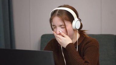 Uzaktan bilgisayar oyunu oynayan, zihinsel yorgunluk yaşayan, kulaklık takan ve yorgunluk belirtileri gösteren profesyonel serbest çalışan genç kız öğrenci esniyor.