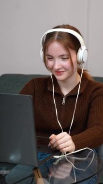 Genç kız öğrenci dizüstü bilgisayara konsantre oluyor, çalışırken müzik dinliyor, ve ev ortamında uzaktan çalışırken konsantre oluyor.