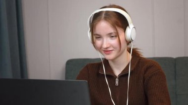 Genç kız öğrenci dizüstü bilgisayara konsantre oluyor, çalışırken müzik dinliyor ve rahat bir ev ortamında uzaktan çalışırken konsantre oluyor.