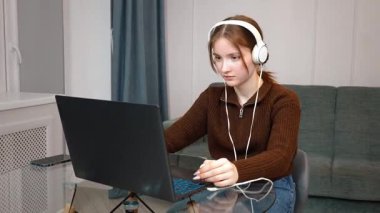 Genç kız öğrenci dizüstü bilgisayara konsantre oluyor, çalışırken müzik dinliyor ve rahat bir ev ortamında uzaktan çalışırken konsantre oluyor.