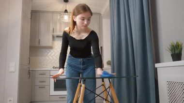 Genç kız cam masa yüzeyini iyice temizliyor, modern mutfak içinde kusursuz parlaklık sağlıyor, titiz hijyen ve ev işleri hassasiyetini gösteriyor.