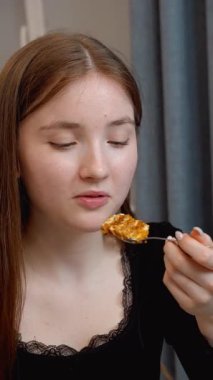 Genç bir kız bilgisayardaki çevrimiçi içeriği incelerken tatlı tatlının tadını çıkarıyor. Ev mutfağında rahatça oturup dinleniyor.