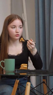 Modern mutfak ortamında, cam masada rahat bir şekilde oturan rahat ofis molası sırasında dizüstü bilgisayar başında çay ve pastanın keyfini çıkaran,