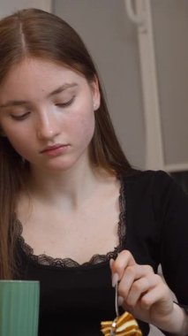 Uzun kahverengi saçlı genç kız kaşıkla yemek yerken çeşitli yüz ifadelerini tecrübe ediyor, otantik duyguları yakalıyor ve yiyeceklerin dikey videolarından zevk alıyor.