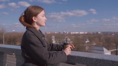 İçkiler ve insanların konsepti. Mutlu genç kadın ya da genç kız. Şehrin arka planında uzun saçlı, şık bir kızla kağıt bardaktan kahve içiyor.